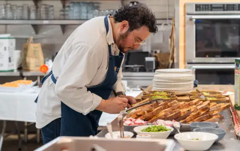 A chef working beside ingredients and prepared food.