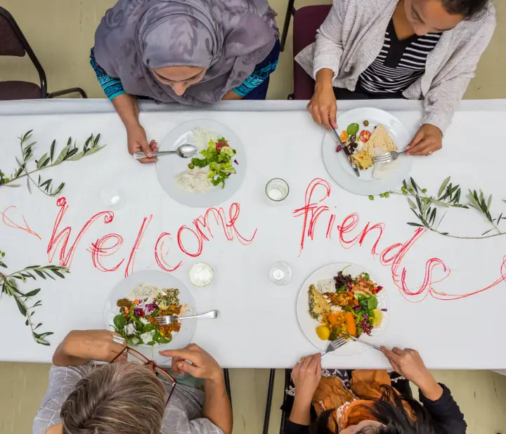 People sharing a meal around a table with a handwritten welcome.