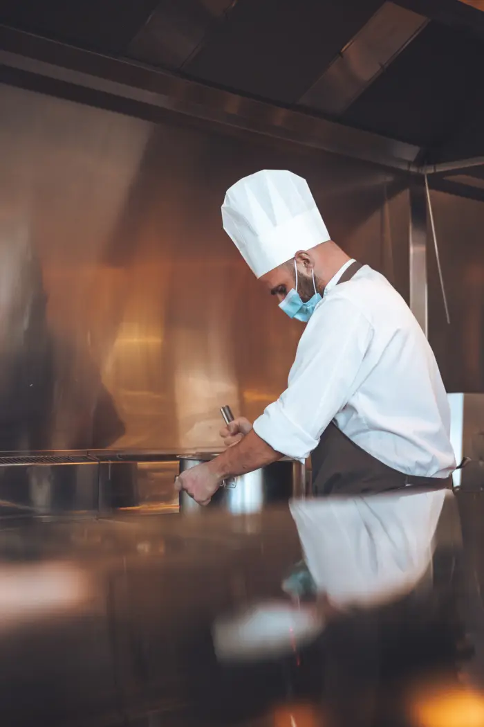 A cook checking work beside a large pot in a professional kitchen.